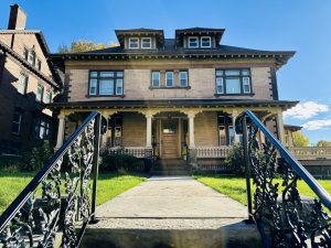 Brick two-story house with a front porch and decorative black metal railings along the walkway to the entrance on a sunny day