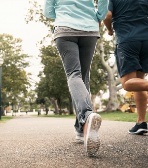 Two people jogging on a park path, viewed from behind in athletic clothing.