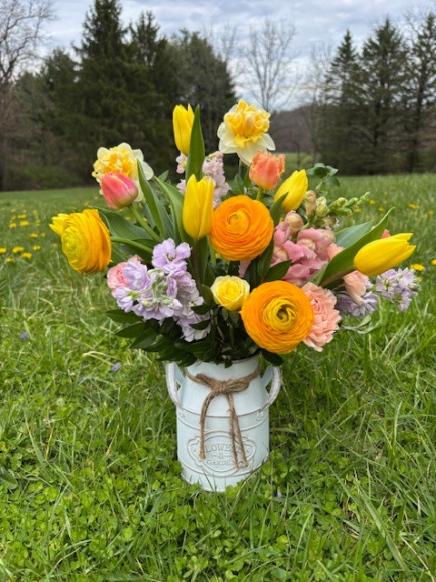Colorful spring bouquet in a white jar with twine, placed on grass in a sunny field.