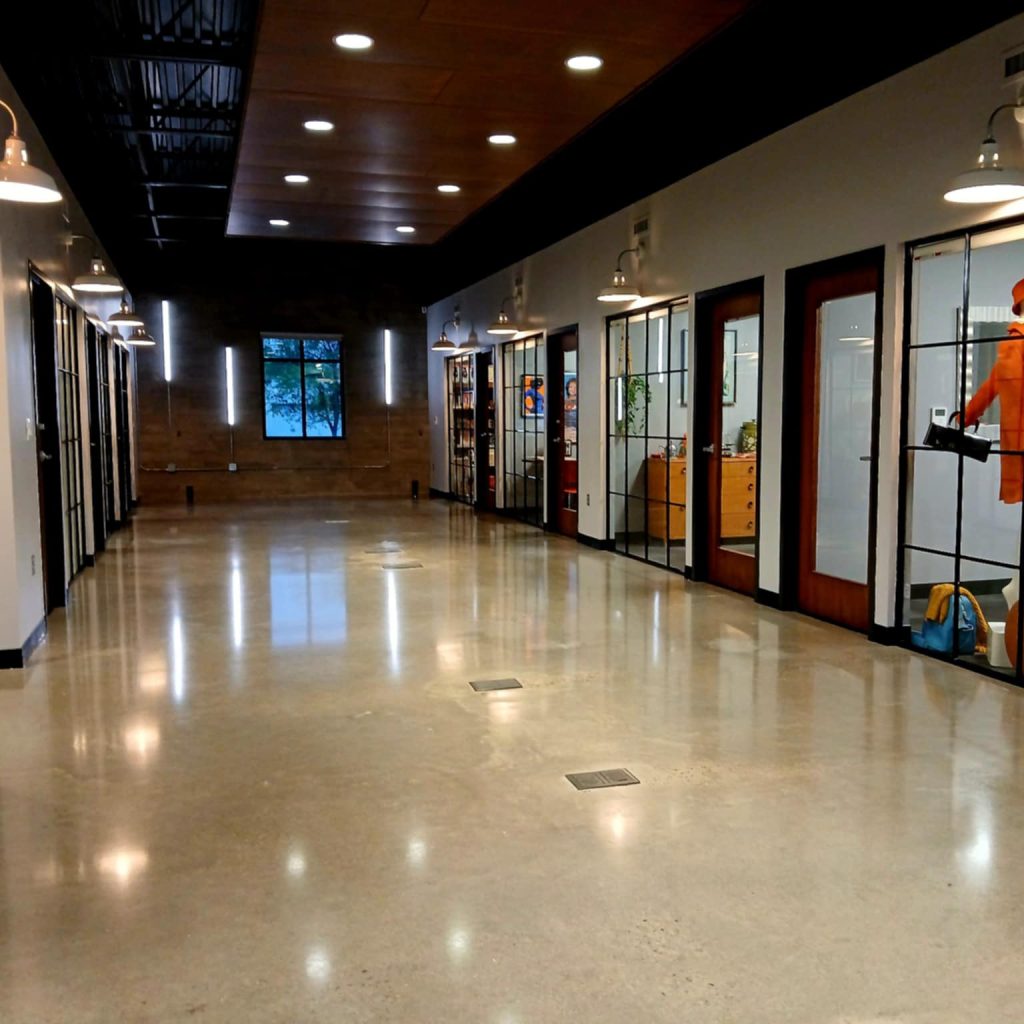 Long indoor hallway with a polished floor, glass-fronted offices lining the right, and bright ceiling lights.