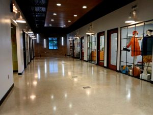 Long indoor hallway with a polished floor, glass-fronted offices lining the right, and bright ceiling lights.