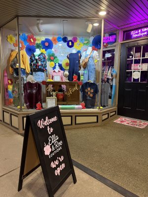 Boutique storefront display with colorful paper flowers and mannequins wearing outfits in the Ella & Roo Boutique window display, plus a welcome sign.